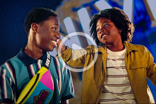 A video play button over a young Guest and his older brother smiling at each other in front of the glowing Universal globe.