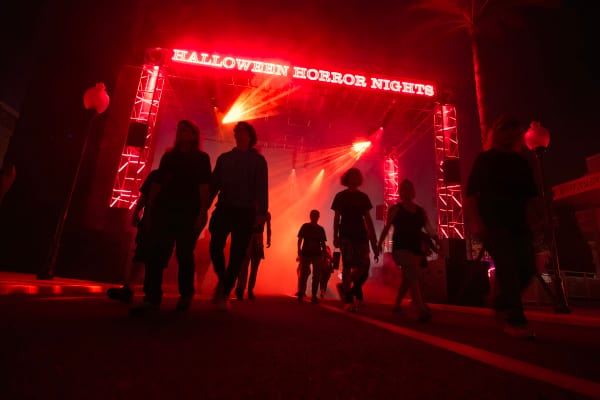 An image of people walking through the park entrance under a glowing red 'HALLOWEEN HORROR NIGHTS' sign at night.