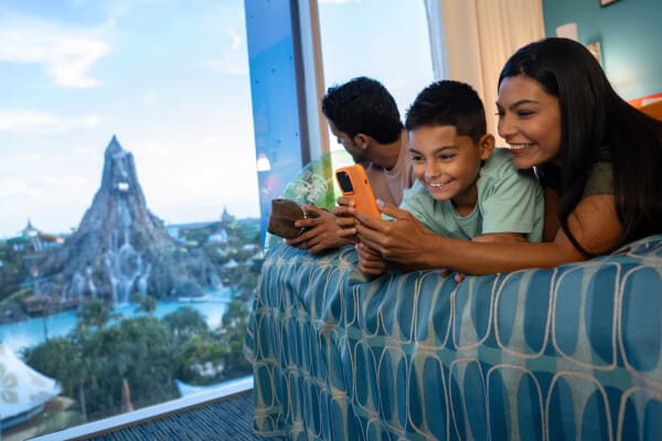 A happy family of three relaxing in their hotel room at Cabana Bay Beach Resort overlooking Volcano Bay.