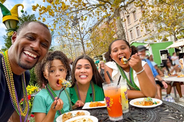 A family wearing colorful Mardi Gras beads and enjoying food during Universal Mardi Gras.