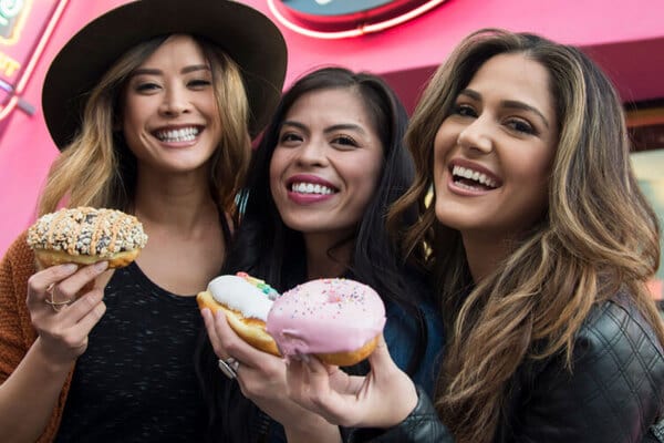 3 women smiling together holding up Voodoo doughnuts