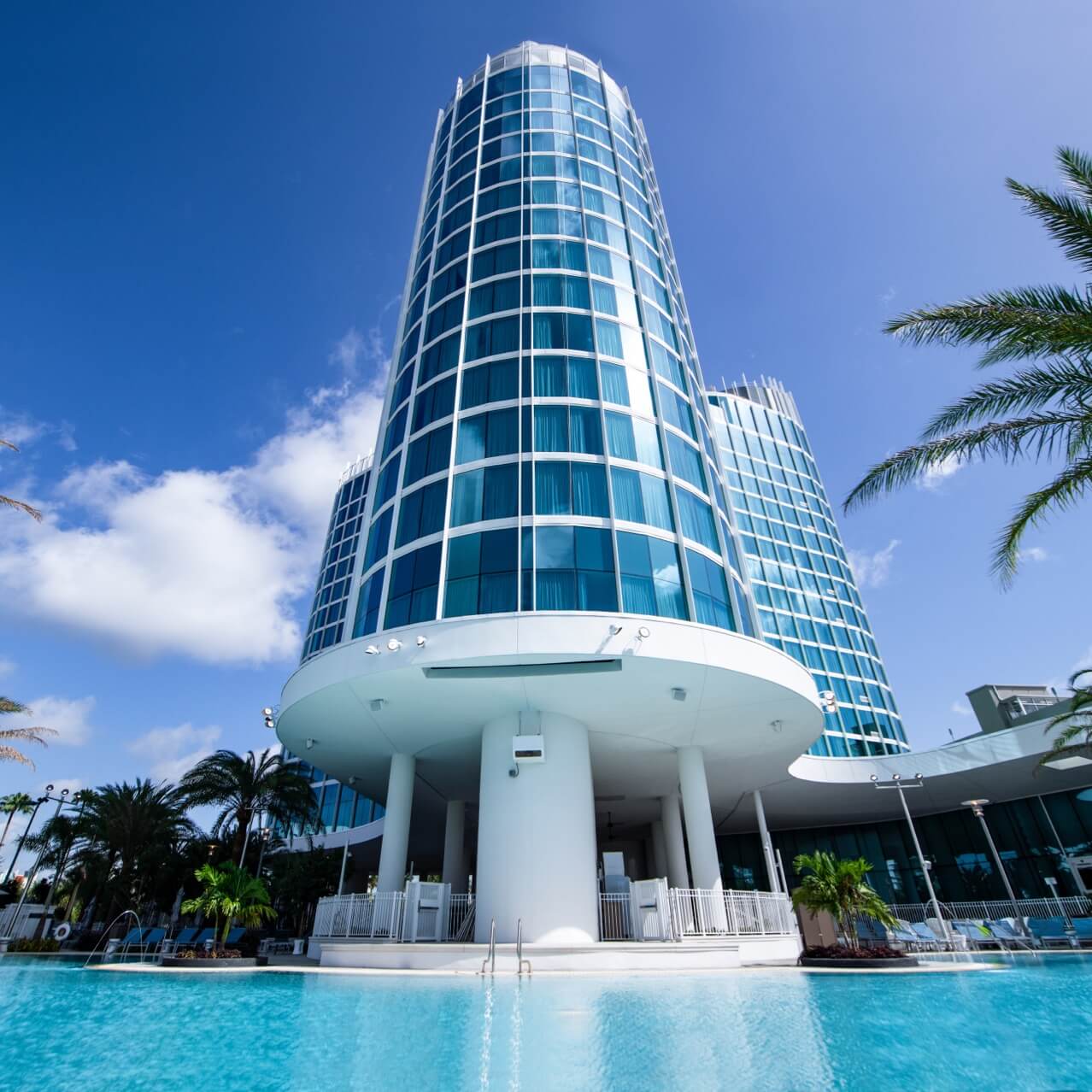 The sleek white and glass tower of Universal's Aventura Hotel overlooks a crystal blue pool.