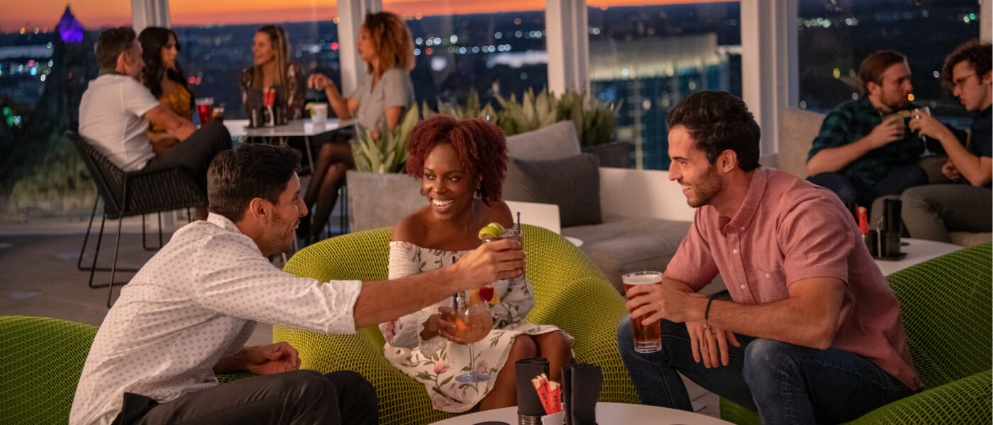 Friends toast their drinks from the Bar 17 Bistro rooftop bar at Aventura Hotel.