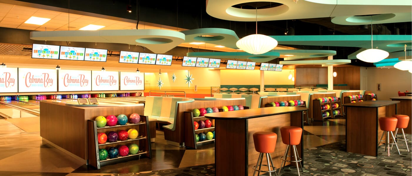 The interior of Galazy Bowl at Cabana Bay Beach Resort in Universal Orlando, a classic bowling alley inspired by classic cinema, complete with space age patterned carpet, mid century modern decor, and a bevy of bright bowling balls.