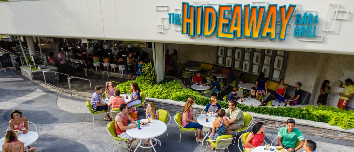 Guests enjoying snacks, meals, and drinks at outdoor dining tables at the Hideaway Bar & Grill in Universal Orlando's Cabana Bay Beach Resort.
