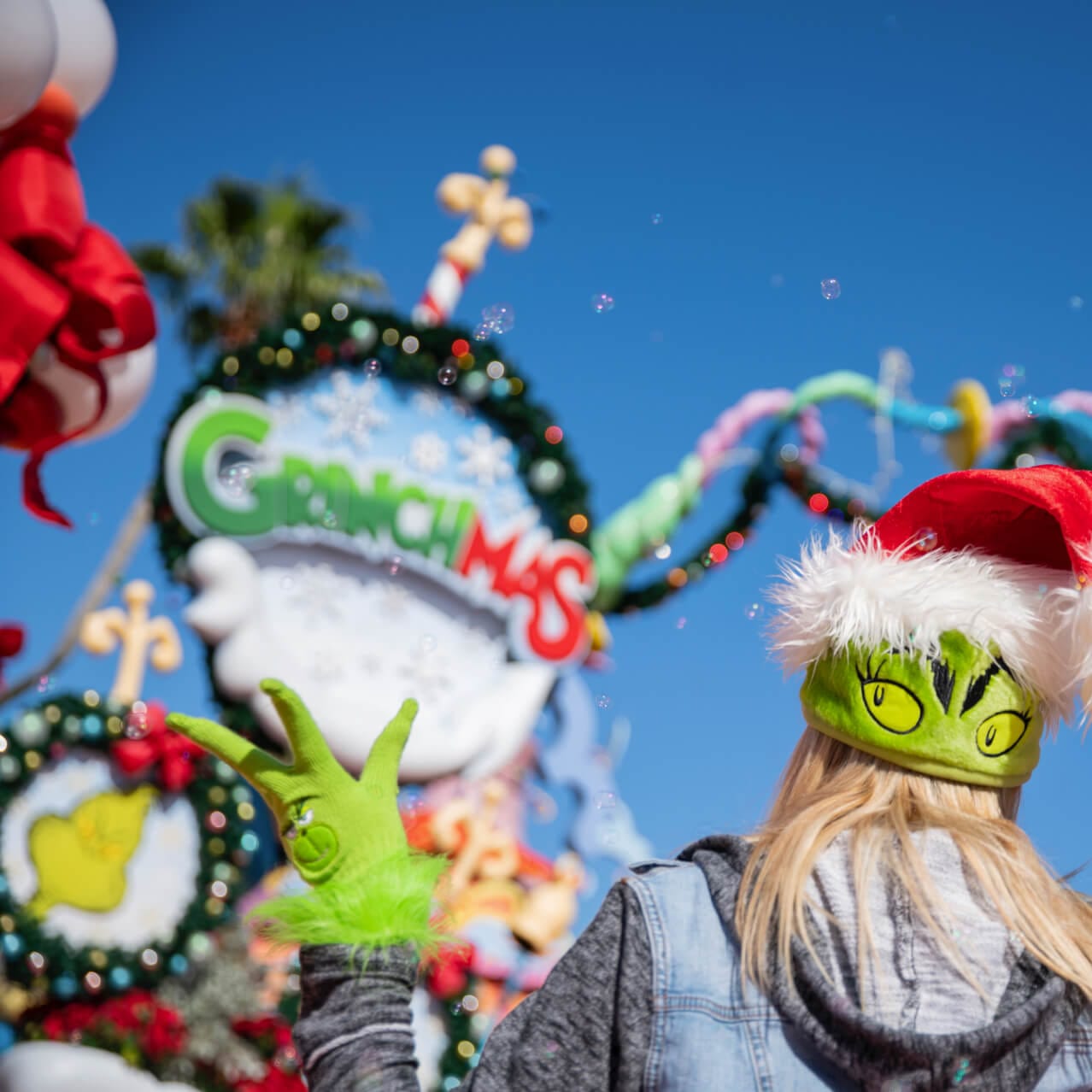 The back of a person wearing a Grinch Santa hat and Grinch gloves during Grinchmas at Universal Orlando.