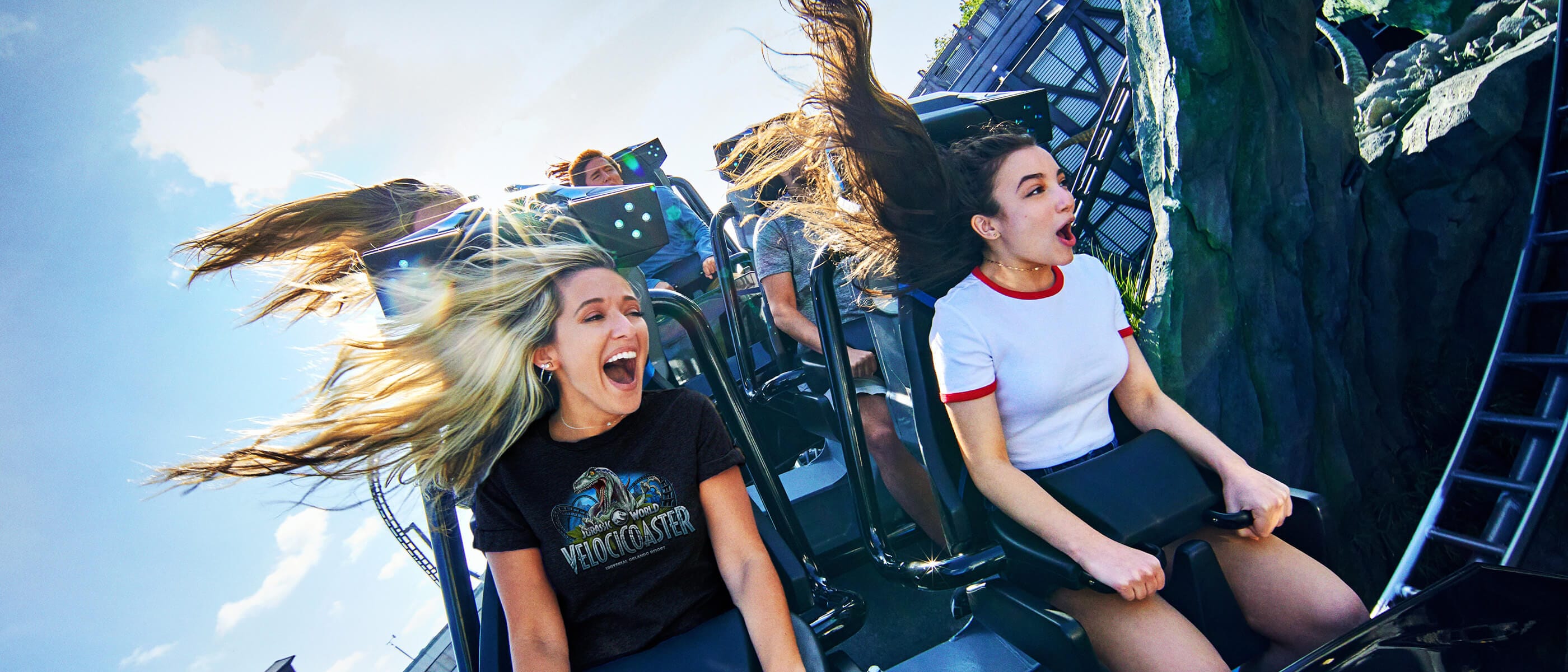 Two girls scream and smile as they grip the handles on the VelociCoaster ride at Universal Islands of Adventure.