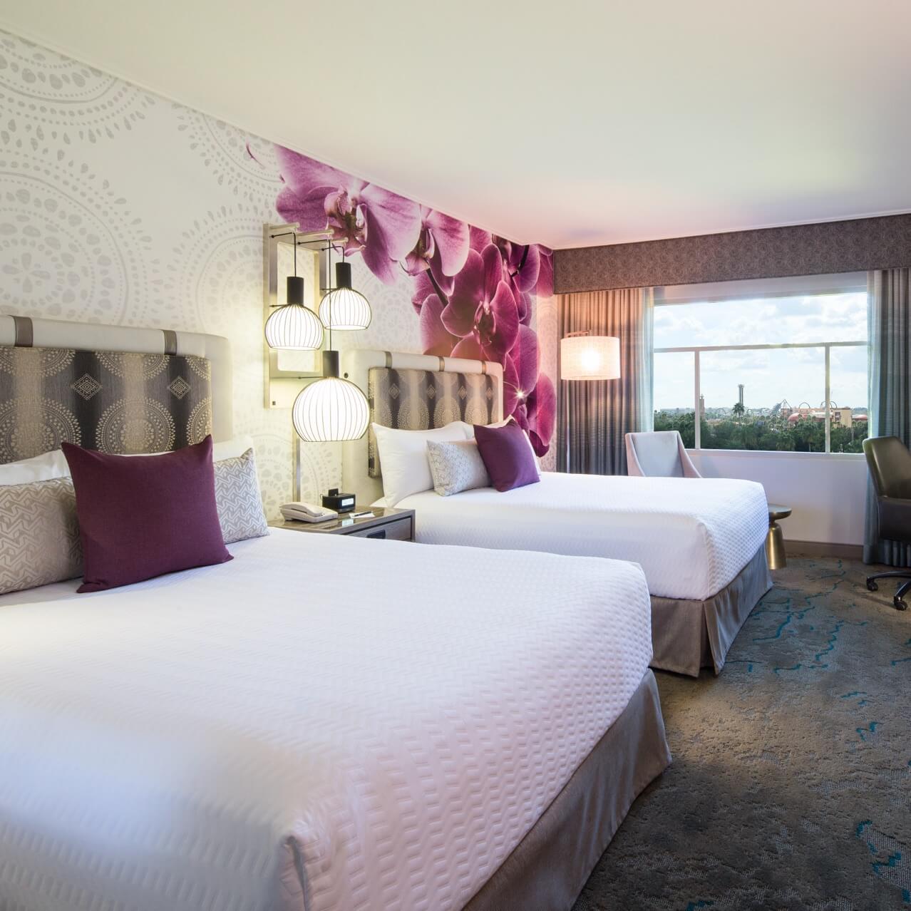 The interior of a Two Queen Guest Room at Loews Royal Pacific Resort with large, modern orchid wallpaper inspired by the South Seas and fresh furniture and decor. 