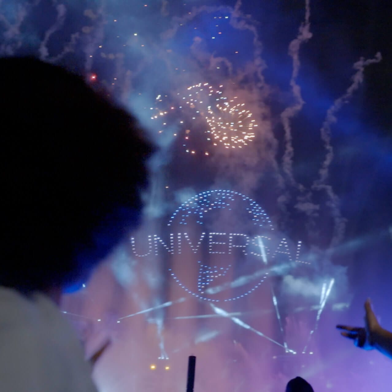Guests watch a fireworks display and drones perform, creating the Universal globe against the dark sky at Universal Epic Universe.