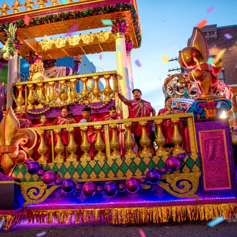 Guests wave and throw beads from atop a parade float at Universal's Mardi Gras: International Flavors of Carnaval.