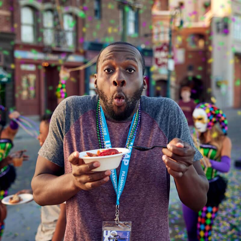 A man wearing a Universal Orlando Passholder lanyard makes a surprised face as he tries spicy Mardi Gras food.