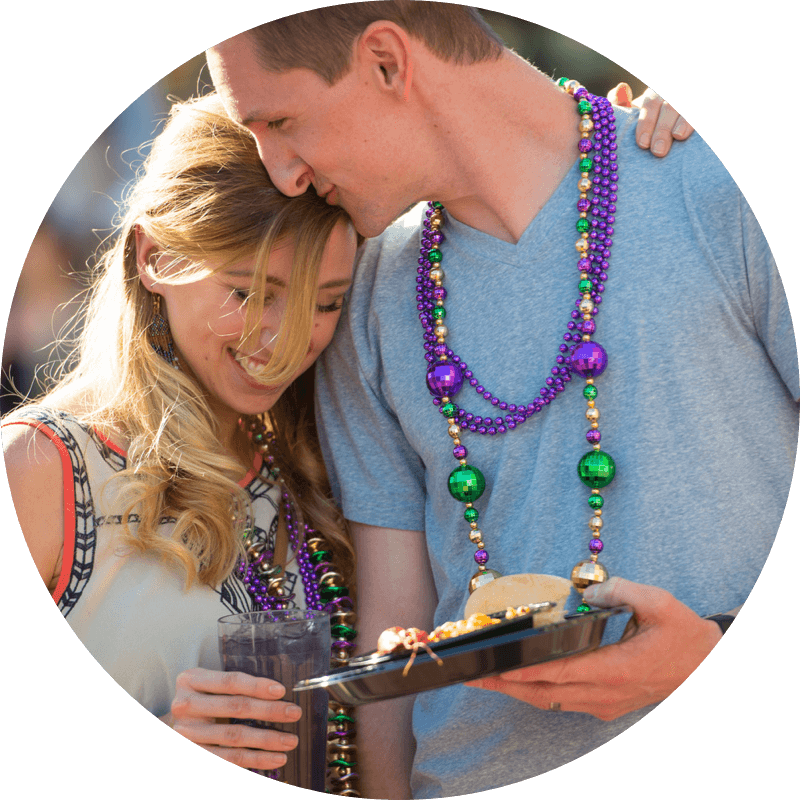 A man kisses a woman's head as they hold Mardi Gras food in the streets of Universal Studios.
