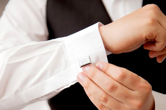 A waiter in a white shirt and black vest fixes his cufflinks.