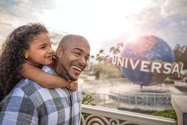 A father laughs as he gives his young daughter a piggy back ride through the park.