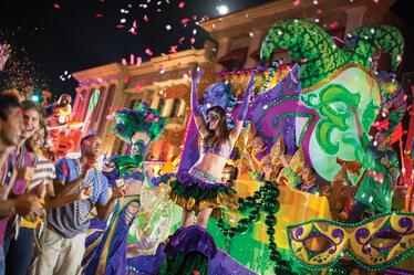 A Mardi Gras performer greets a happy crowd in front of a colorful float.