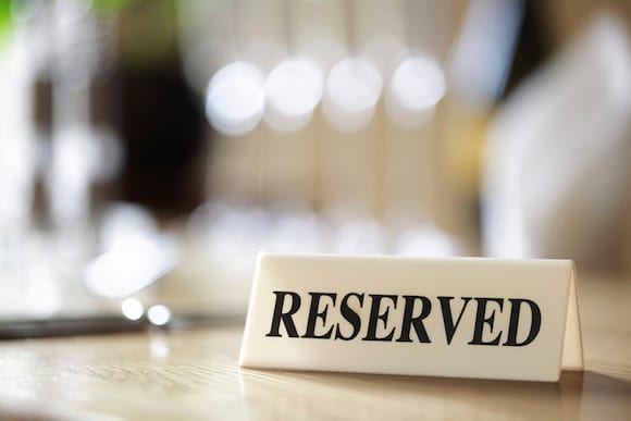 A white sign with black lettering that reads 'RESERVED' sits on a tabletop.
