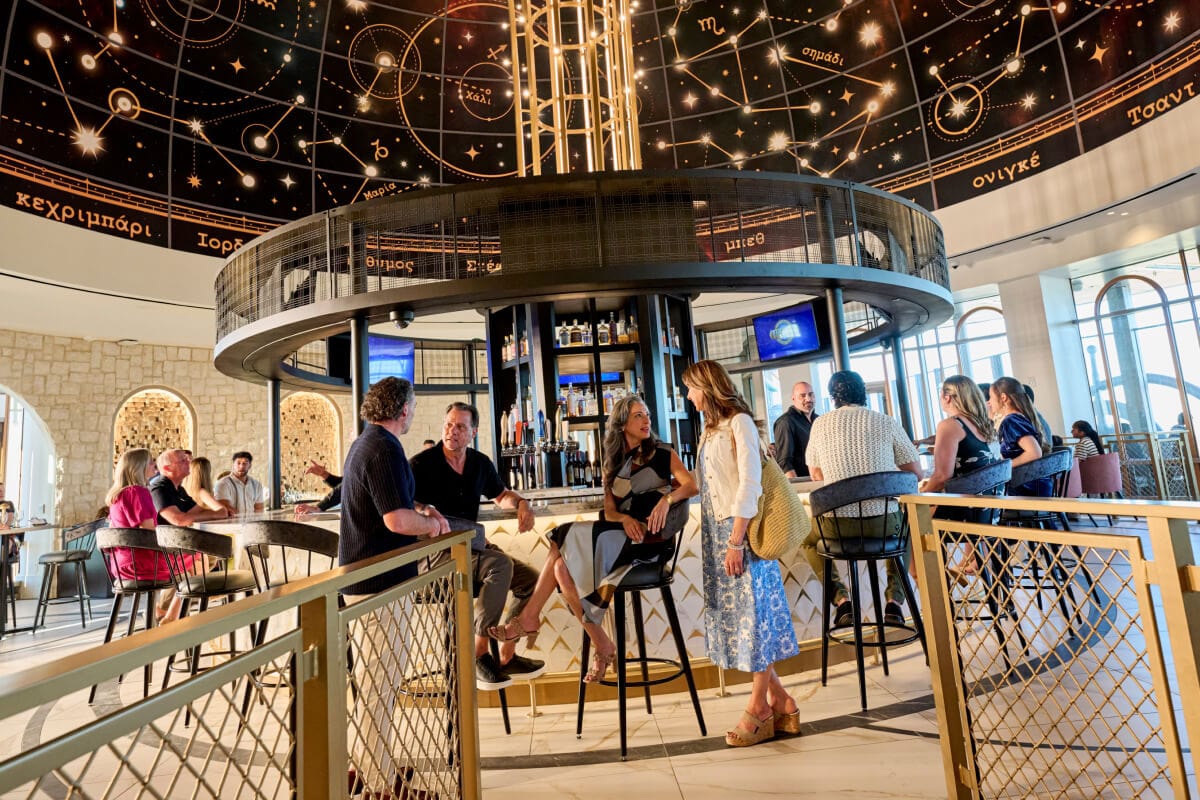 Guests enjoying conversation at the center bar of Bar Helios, inside Universal Helios Grand Hotel.