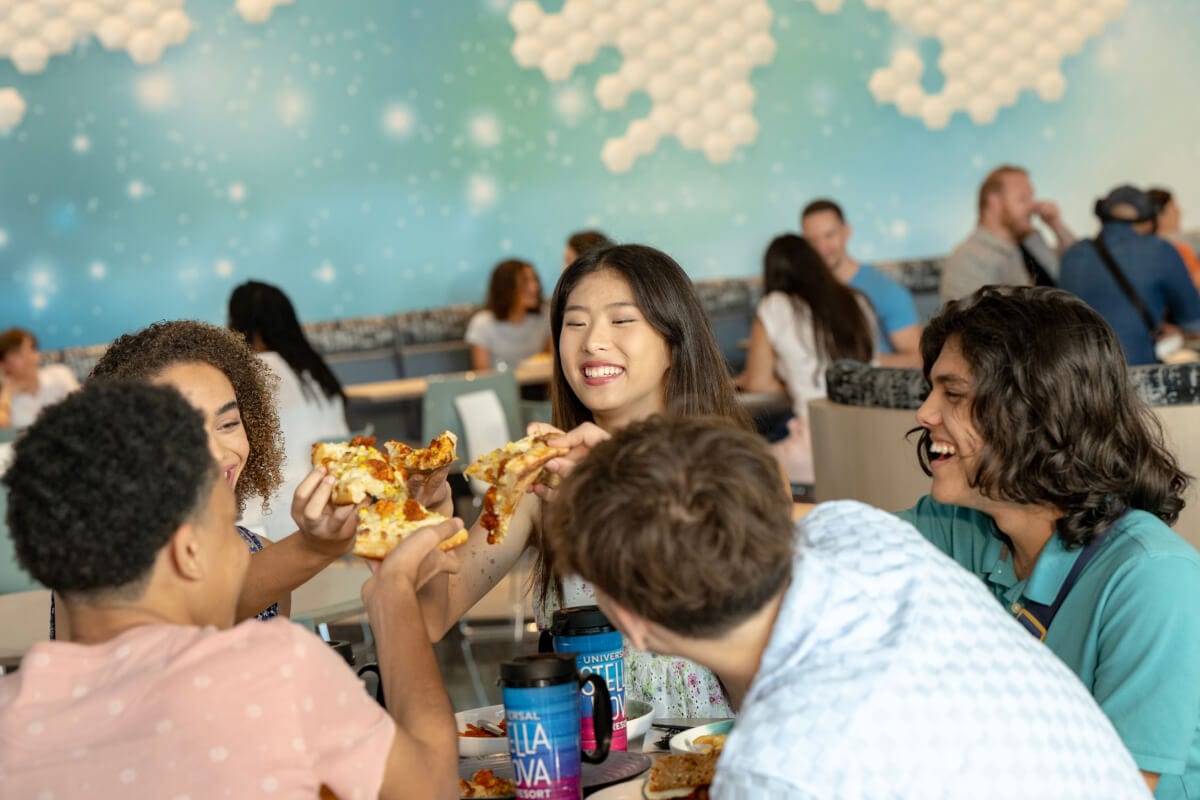 Five friends enjoying food and drinks inside of the Cosmos Cafe and Market at Universal Stella Nova Resort.