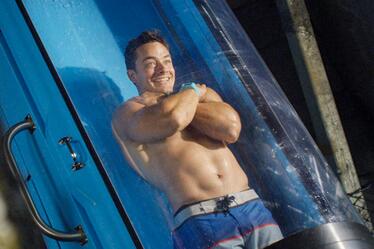 Image of young man in bathing suit rapidly descending water drop-slide.