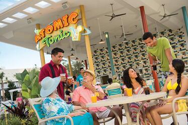 Ubicado en el área de la piscina del Cabana Courtyard, este bar de Universal Orlando sirve bebidas no alcohólicas ademas de vino, cerveza y tragos refrescantes. Un mesero le sirve a visitantes sentados en una mesa afuera de Atomic Tonic, un bar al aire libre estilo retro en Universal's Cabana Bay Beach Resort.