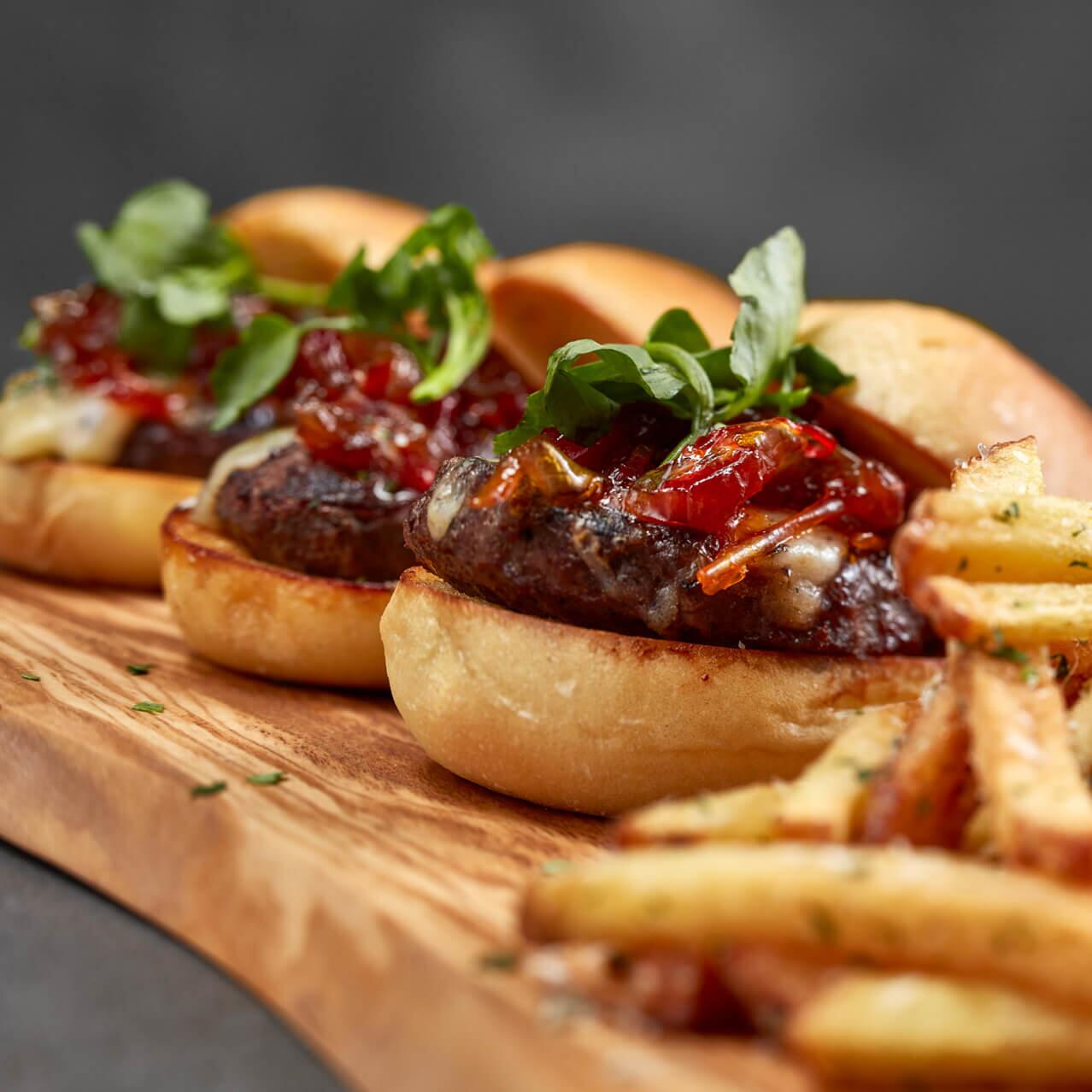 Tres minihamburguesas de carne de res servidas con papas fritas en un tablero de madera en Bar 17 Bistro en Universal's Aventura Hotel.