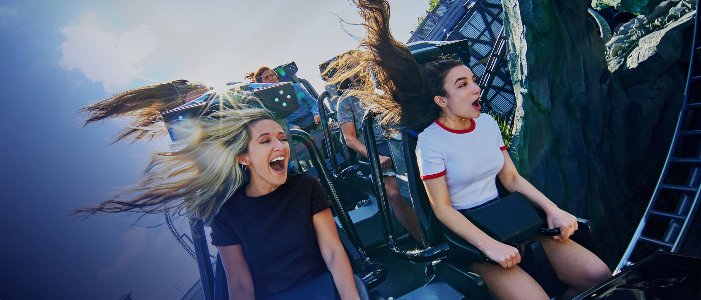Two girls scream and smile as they grip the handles on the VelociCoaster ride at Universal Islands of Adventure.