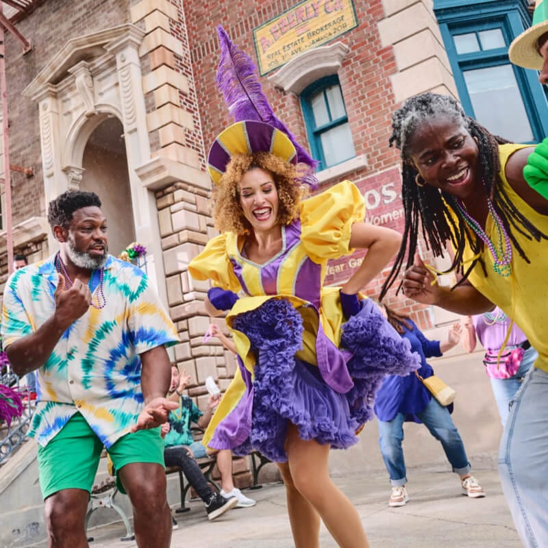 Una familia baila con artistas disfrazados mientras disfrutan de Universal Mardi Gras: Festival de Sabores del Mundo.