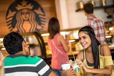 Disfruta de un café por la mañana o de una bebida helada por la tarde en el local de Starbucks del Cabana Bay Beach Resort, un hotel de categoría Prime Value dentro del complejo de Universal Orlando. Una pareja disfruta bebidas sentados en una mesa en Starbucks.